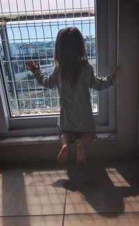 Rear view of girl looking through window at home