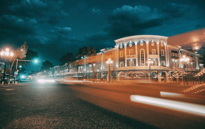 Illuminated building by street against sky at night