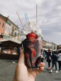 Close-up of woman holding ice cream against sky on street