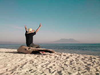 Man gesturing peace sign while sitting at beach against sky