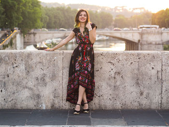 Portrait of smiling young woman standing on retaining wall