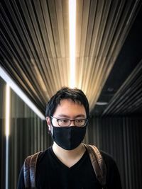 Portrait of a young man standing against ceiling and wall.