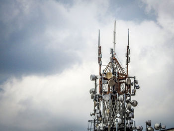 Close-up of communications tower against cloudy sky in city