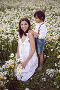 Woman in a white dress with her son  in a chamomile field at sunset in summer