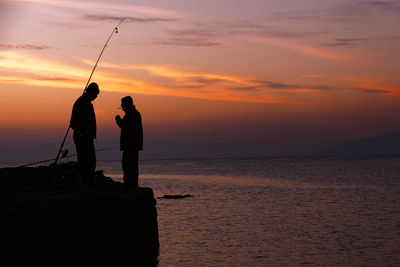 Silhouette men fishing in sea during sunset