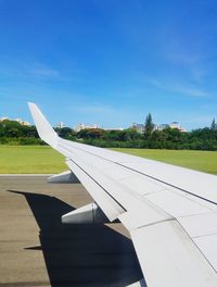 Close-up of airplane wing on runway against blue sky