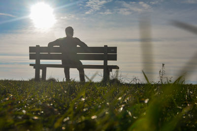 Rear view of man sitting on field against sky during sunset