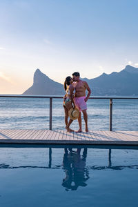 Full length of couple embracing against sea and sky