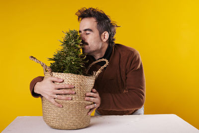 Side view of young man sitting against yellow background