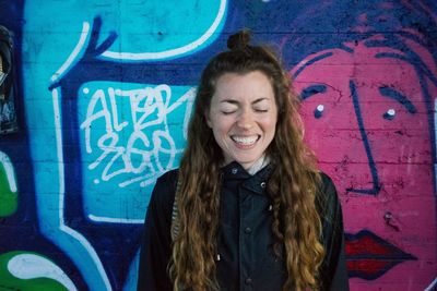Young woman laughing against graffiti on wall