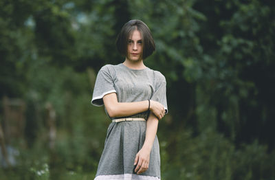 Portrait of beautiful young woman standing against trees