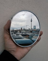 Cropped image on hand holding mirror with reflection of fernsehturm and cityscape