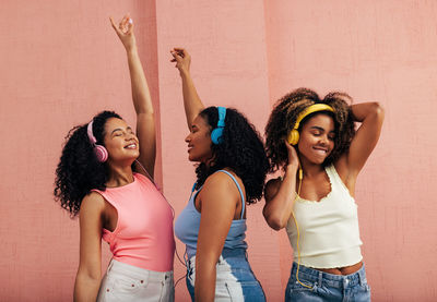 Female friends enjoying music against wall