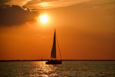 Silhouette sailboat sailing on sea against sky during sunset