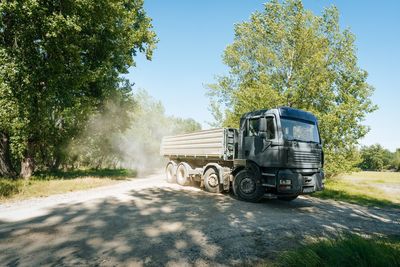 Truck on dusty road by trees against sky