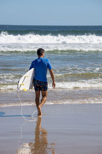 Rear view of man with surf board at beach against sky