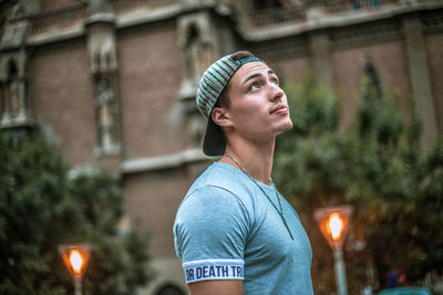 Thoughtful young man wearing cap while standing against building