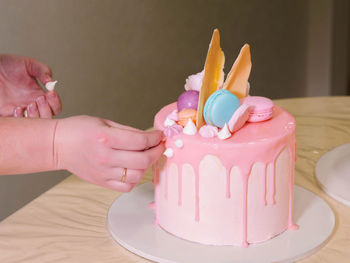 Cropped hands of woman decorating cake on table at home