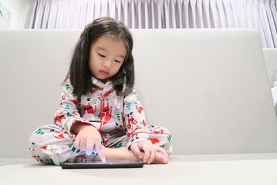 Cute asian girl looking down and playing game on mobile phone while sitting against wall