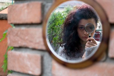 Young woman holding magnifying glass reflecting on mirror