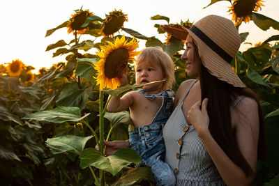 Beautiful mother holds a little son in her arms in a field of sunflowers at sunset