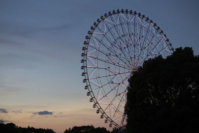 Low angle view of ferris wheel and silhouette trees against sky