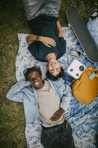Directly above portrait of happy teenage boy lying down with male friend on picnic blanket in park