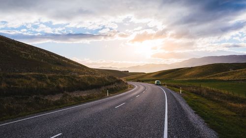 Road leading towards mountains against sky during sunset