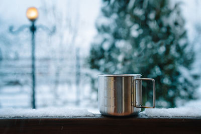 Close-up of a travel steel mug with coffee on snowy table in a winter morning