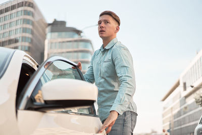 Young man standing on car in city