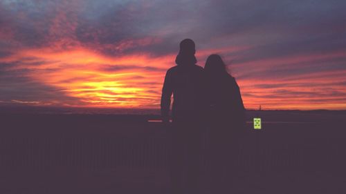 Silhouette couple standing at beach against orange sky during sunset