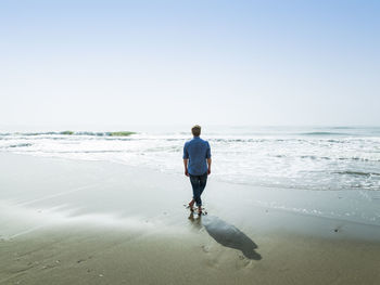 Rear view of man on beach against clear sky