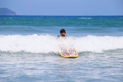 Portrait of boy surfing in sea against sky