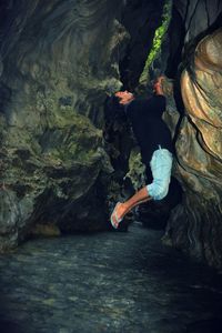 Man climbing on rock over river in forest