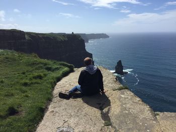 Rear view of woman sitting on rocks by sea