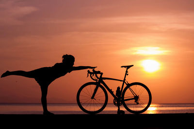 Silhouette person riding bicycle against sky during sunset