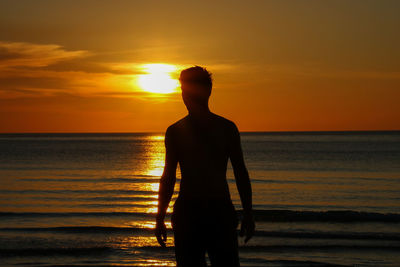 Rear view of silhouette man standing on beach during sunset