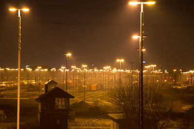 Illuminated street lights by buildings against sky at night