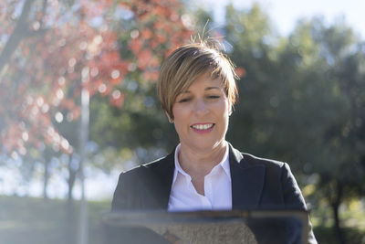 Portrait of young businesswoman standing against trees