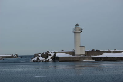 Lighthouse by sea against clear sky