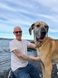 Portrait of happy man with great dane on shore against sky