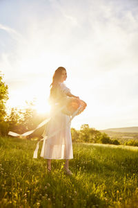 Side view of woman standing on field against sky during sunset