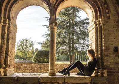 Side view of young woman sitting on arch window