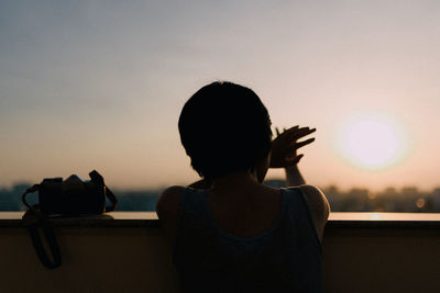 Rear view of woman sitting against sky during sunset