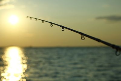 Close-up of silhouette fishing rod against sea at sunset