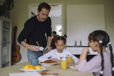 Father serving cheese spread to daughter having breakfast at dining table in home