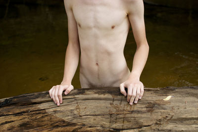 Midsection of naked man standing by wood