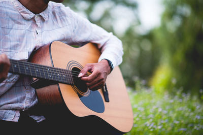 Midsection of man playing guitar against plants