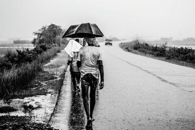 Rear view of men walking on road in rain