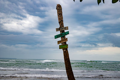 Messages on wooden post at beach against cloudy sky